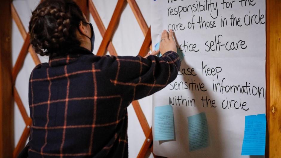 Student inside the UBC Farm yurt standing and pasting a post-it to a sheet of paper on the wall listing climate commitments.
