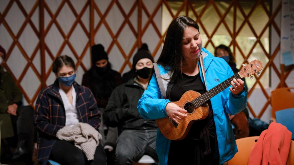 Group of people sitting inside of the UBC Farm yurt. One standing playing the Ukulele. 