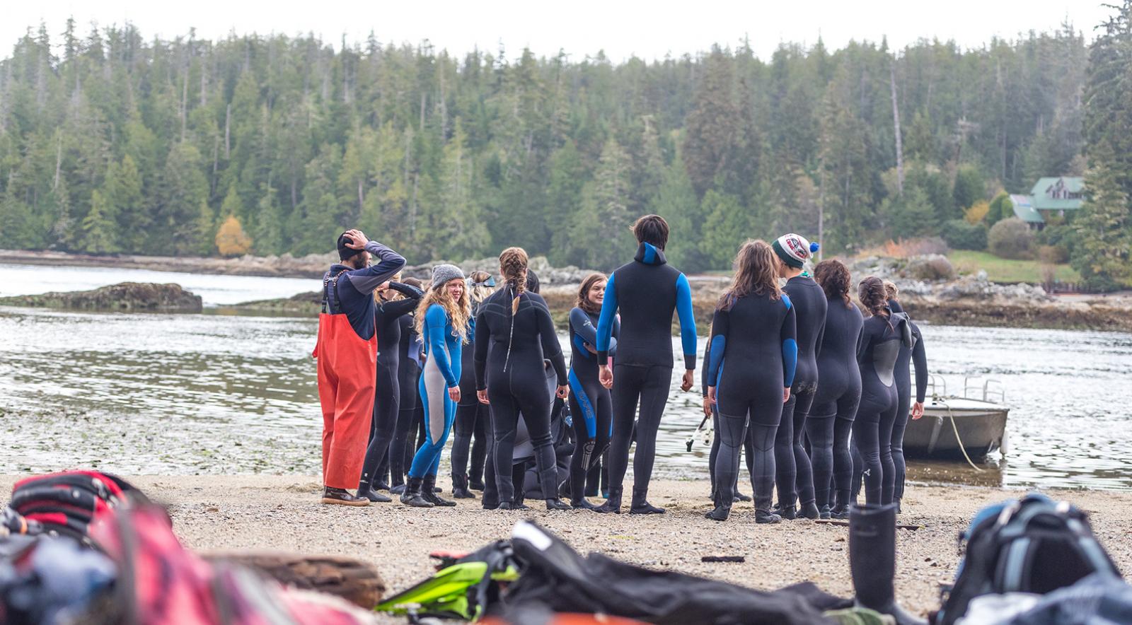 Group of students in wetsuits on shoreline by the ocean